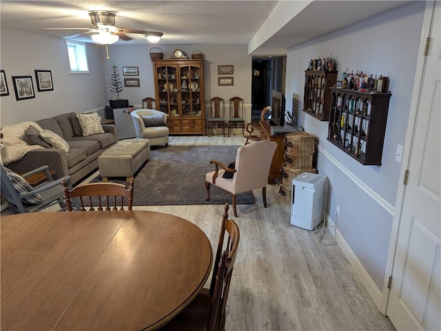 living room with baseboards, a textured ceiling, a ceiling fan, and wood finished floors