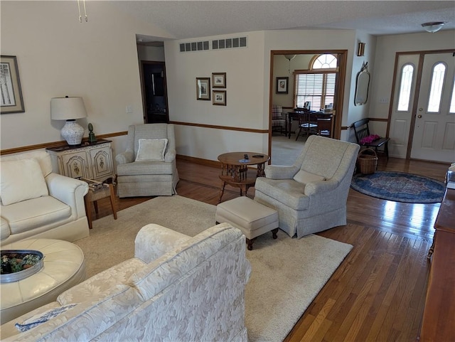 living area featuring visible vents, baseboards, a textured ceiling, and hardwood / wood-style floors