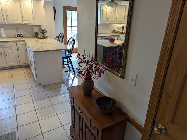 kitchen with a breakfast bar area, light stone counters, a peninsula, light tile patterned flooring, and white cabinetry