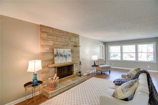 living room with a stone fireplace, a textured ceiling, and hardwood / wood-style flooring