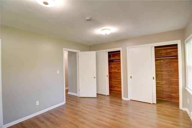 unfurnished bedroom with a textured ceiling, light wood-type flooring, two closets, and wood walls