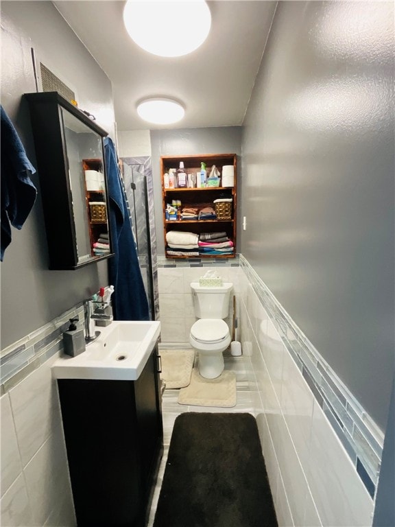 bathroom featuring tile patterned floors, vanity, toilet, and tile walls