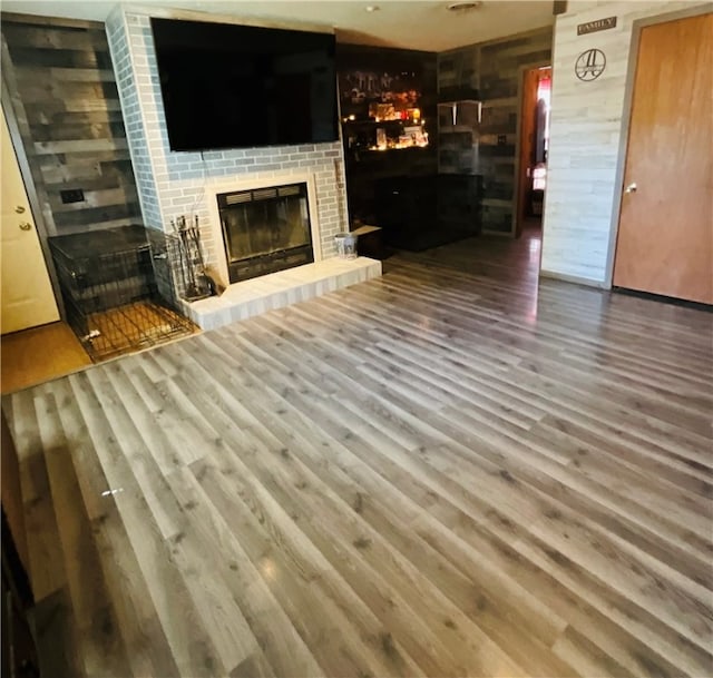 unfurnished living room with wood-type flooring and a brick fireplace