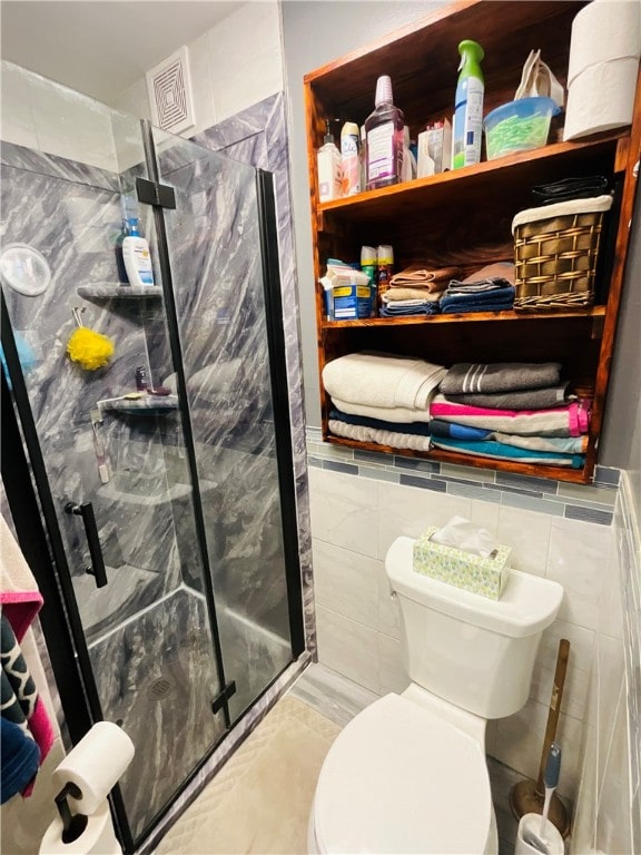 bathroom with toilet, a shower with shower door, and tile walls