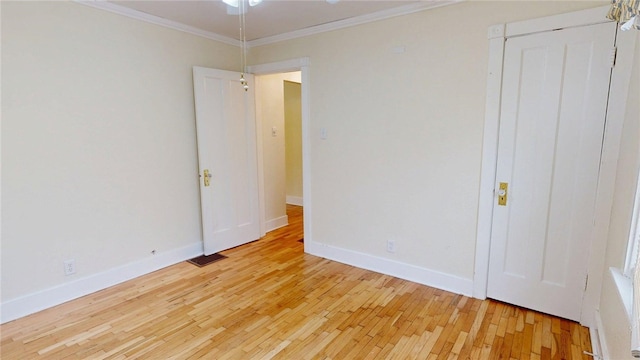 spare room featuring crown molding, light wood-type flooring, ceiling fan, baseboards, and visible vents