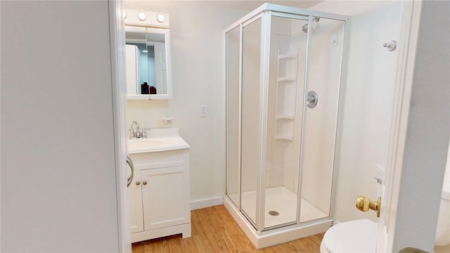 bathroom featuring toilet, vanity, wood finished floors, and a stall shower