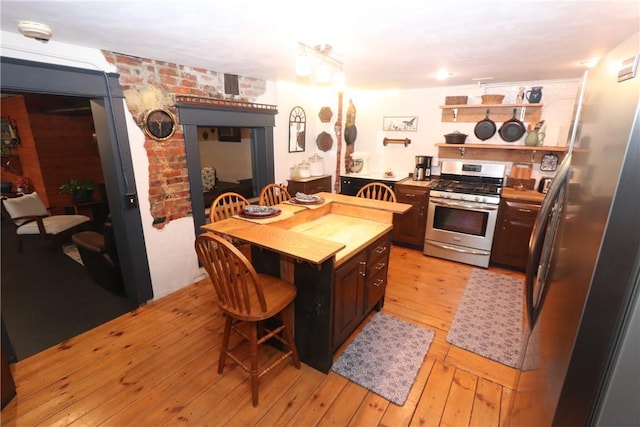 kitchen with stainless steel appliances, a kitchen breakfast bar, dark brown cabinets, and light wood-type flooring