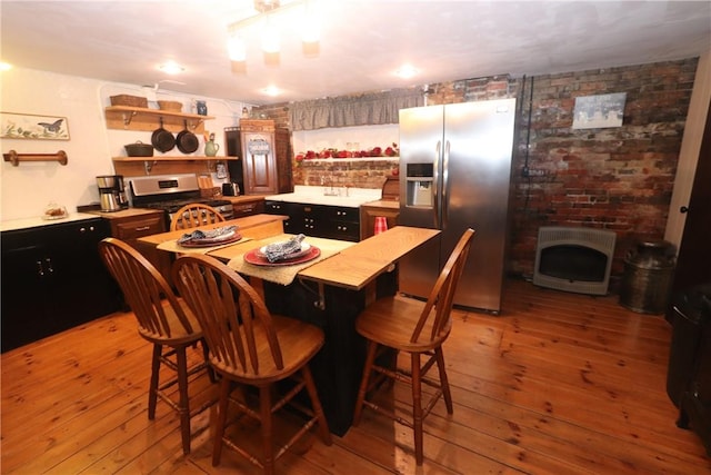 kitchen featuring appliances with stainless steel finishes, heating unit, a fireplace, a center island, and light hardwood / wood-style floors