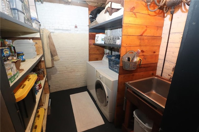 washroom with sink, washer and clothes dryer, and brick wall