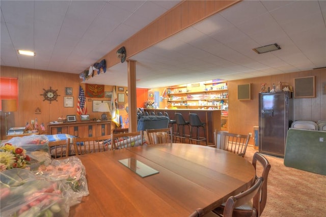 dining room featuring carpet, wooden walls, and a bar