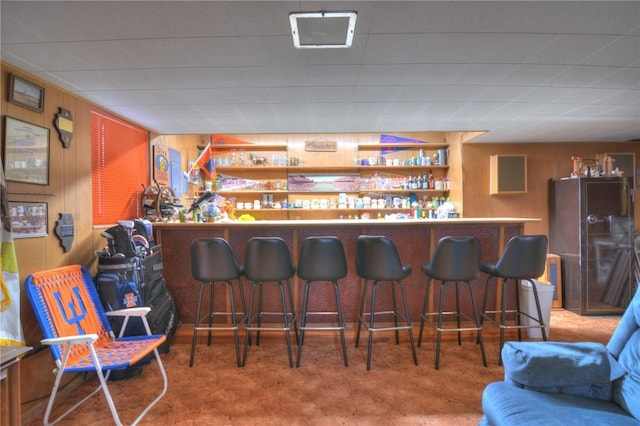 bar featuring carpet floors, a bar, freestanding refrigerator, and wooden walls