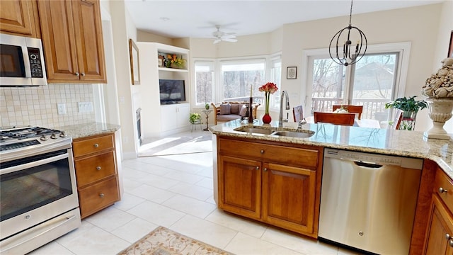 kitchen featuring sink, appliances with stainless steel finishes, light stone countertops, decorative backsplash, and decorative light fixtures