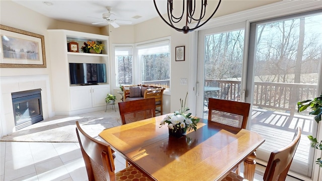 tiled dining area with ceiling fan with notable chandelier and a fireplace