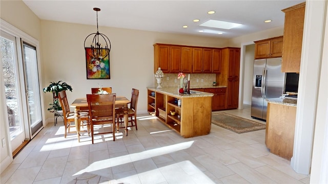 kitchen with tasteful backsplash, stainless steel fridge with ice dispenser, hanging light fixtures, light tile patterned floors, and light stone countertops