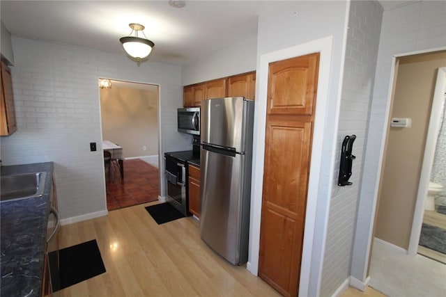 kitchen with brown cabinets, light wood finished floors, stainless steel appliances, dark countertops, and a sink