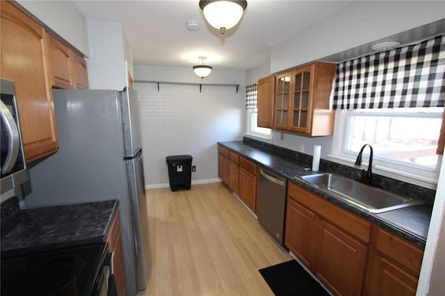 kitchen featuring light wood-style flooring, a sink, stainless steel dishwasher, brown cabinets, and glass insert cabinets