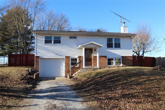 raised ranch with an attached garage, brick siding, fence, driveway, and a chimney