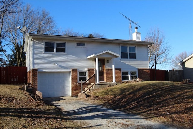 raised ranch featuring a garage, brick siding, fence, and a chimney