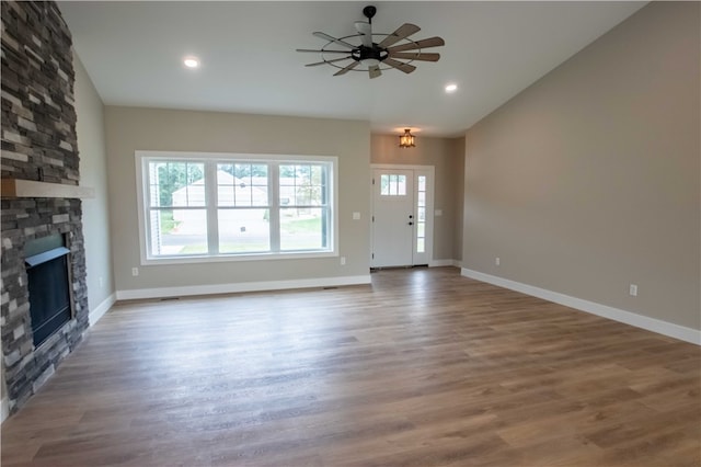 unfurnished living room with hardwood / wood-style floors, ceiling fan, and a stone fireplace