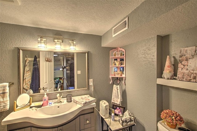 bathroom featuring visible vents, a textured wall, a textured ceiling, and vanity