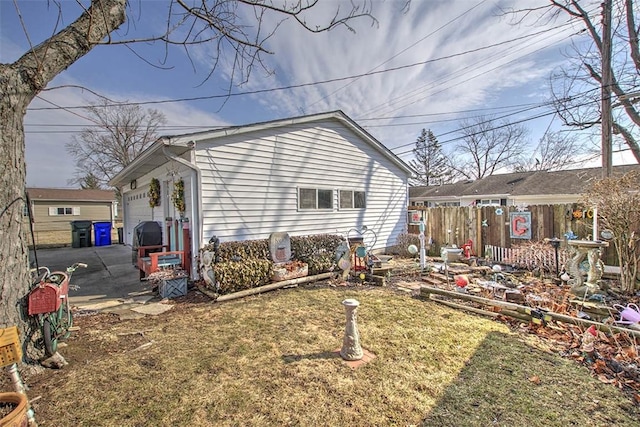 rear view of property featuring a garage, concrete driveway, a lawn, and fence