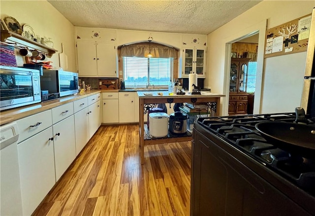 kitchen featuring stainless steel microwave, light wood-style flooring, black range with gas stovetop, and a textured ceiling