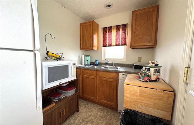 kitchen featuring white appliances, a textured ceiling, dark countertops, brown cabinetry, and a sink