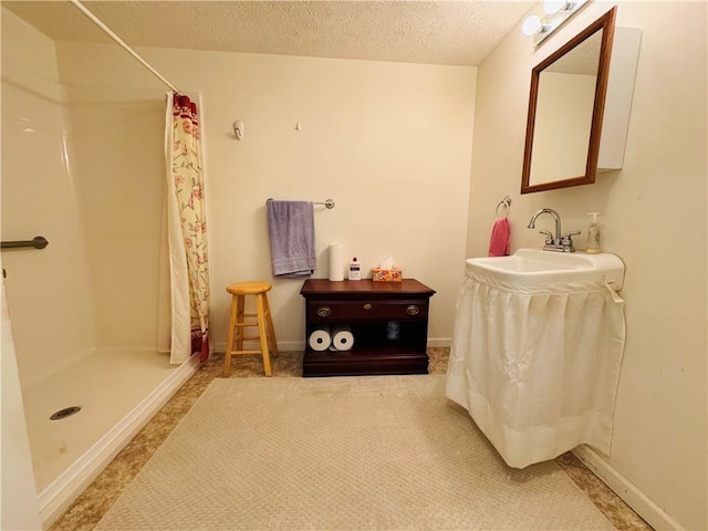 full bath featuring a sink, baseboards, a stall shower, and a textured ceiling