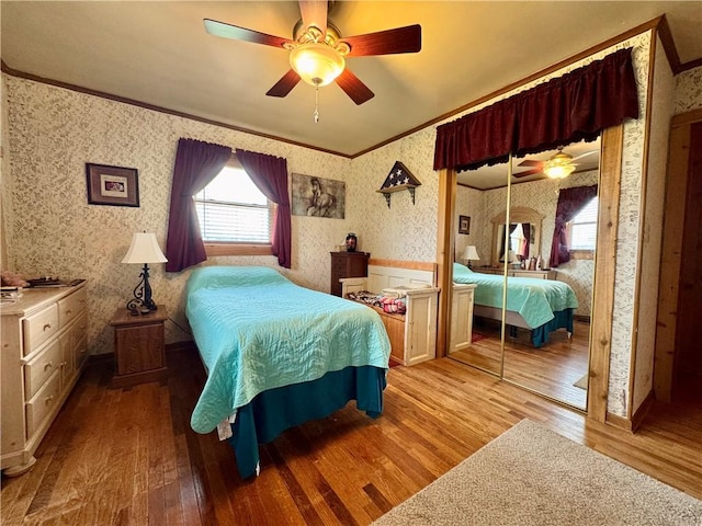 bedroom featuring wallpapered walls, multiple windows, crown molding, and wood finished floors