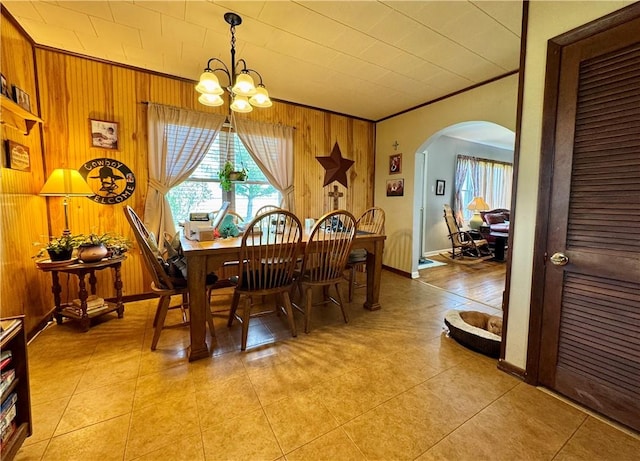 dining space with a notable chandelier, ornamental molding, light tile patterned floors, wood walls, and arched walkways