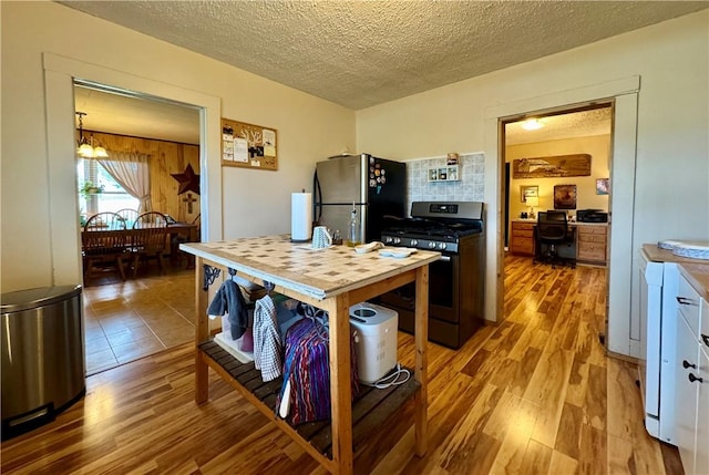 kitchen with a textured ceiling, appliances with stainless steel finishes, a notable chandelier, and light wood finished floors
