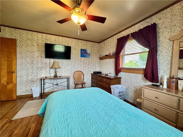bedroom featuring a ceiling fan, crown molding, wood finished floors, and wallpapered walls