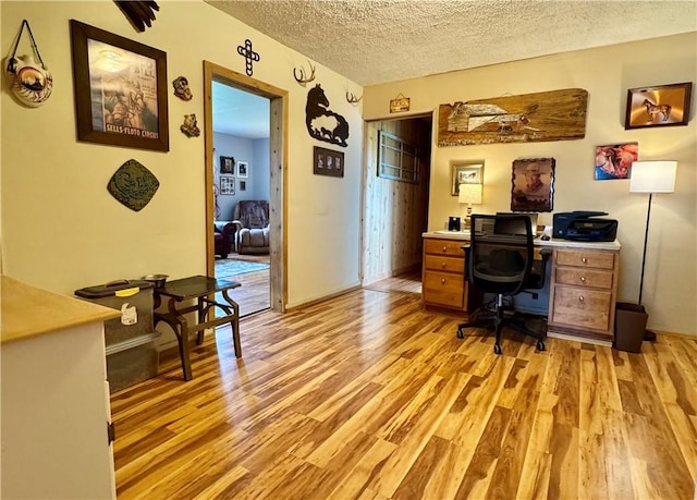 home office with light wood-type flooring and a textured ceiling