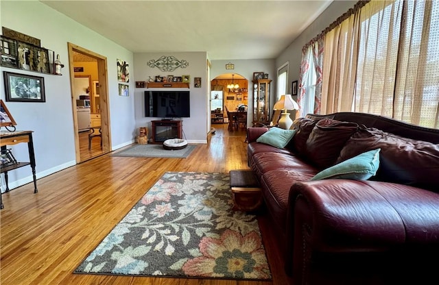 living room with arched walkways, baseboards, an inviting chandelier, and wood finished floors