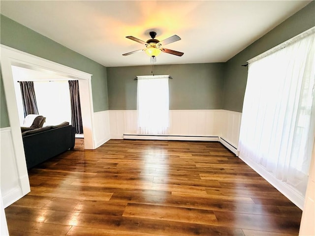 403 S 2nd Ave, Hoopeston, IL 60942 - spare room featuring a ceiling fan, a wainscoted wall, dark wood finished floors, and a baseboard heating unit