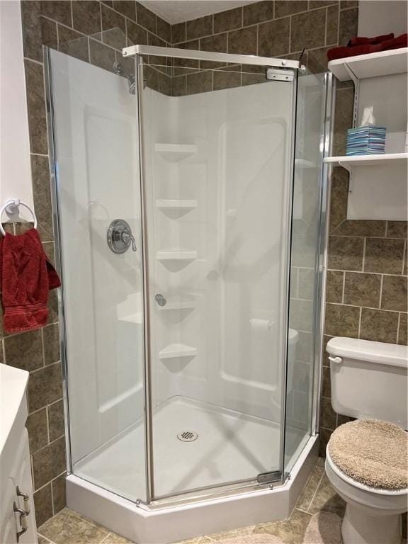 bathroom featuring vanity, toilet, a shower with door, and tile walls