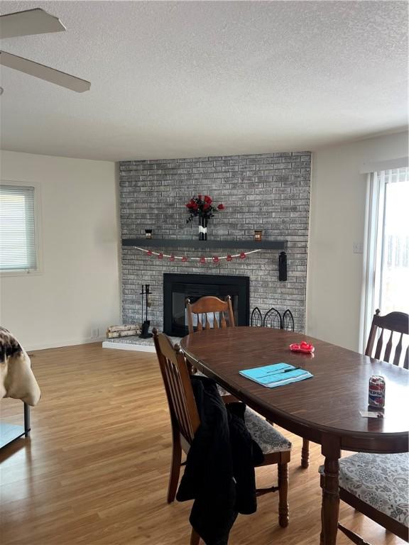 dining space featuring hardwood / wood-style floors, a textured ceiling, a healthy amount of sunlight, and a brick fireplace