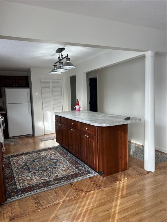 bar featuring dark brown cabinets, white refrigerator, light hardwood / wood-style floors, decorative light fixtures, and ornate columns