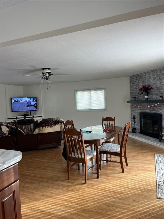 dining space with a brick fireplace, ceiling fan, and light wood-type flooring