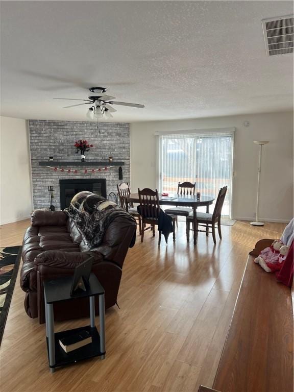 living room featuring ceiling fan, light wood-type flooring, a textured ceiling, and a fireplace