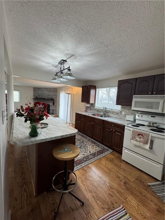 kitchen with sink, a kitchen bar, decorative backsplash, dark brown cabinetry, and white appliances