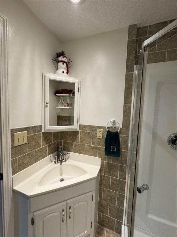 bathroom with walk in shower, vanity, a textured ceiling, and tile walls