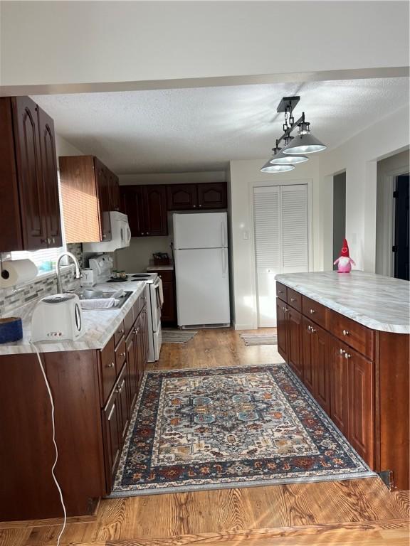 kitchen featuring dark brown cabinetry, sink, hanging light fixtures, light wood-type flooring, and white appliances