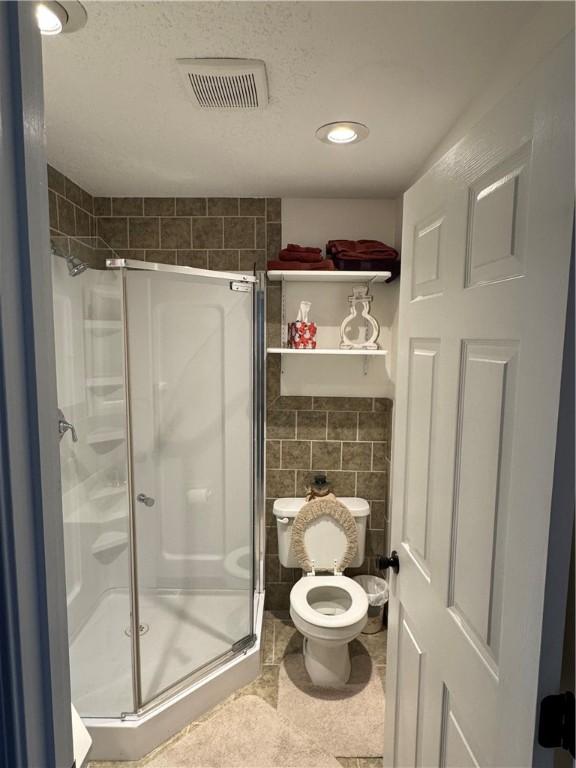 bathroom with toilet, an enclosed shower, and tile walls