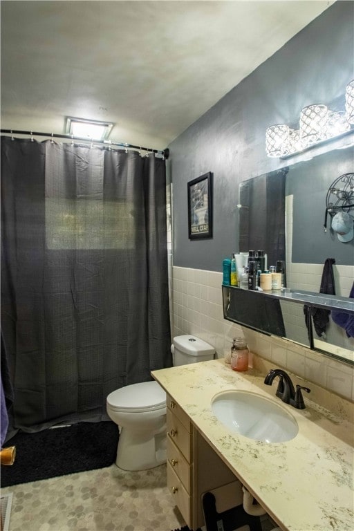 bathroom with curtained shower, vanity, tile walls, and toilet