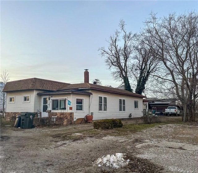 rear view of property featuring a shingled roof and a chimney