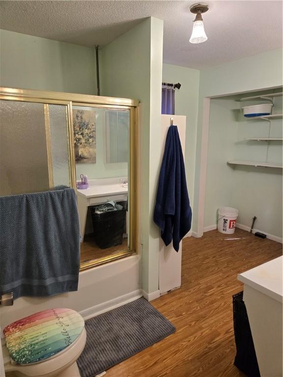 full bath featuring a textured ceiling, baseboards, wood finished floors, and a shower with shower door