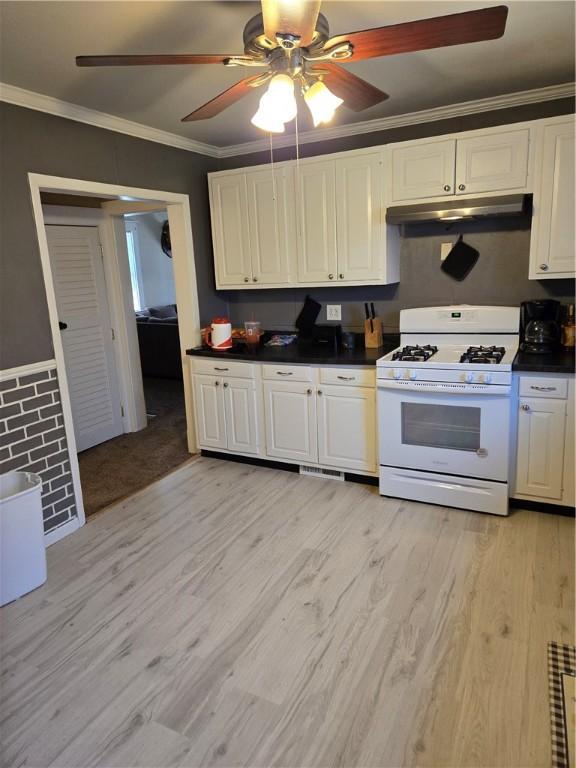 kitchen with white gas range oven, dark countertops, light wood-style flooring, ornamental molding, and under cabinet range hood