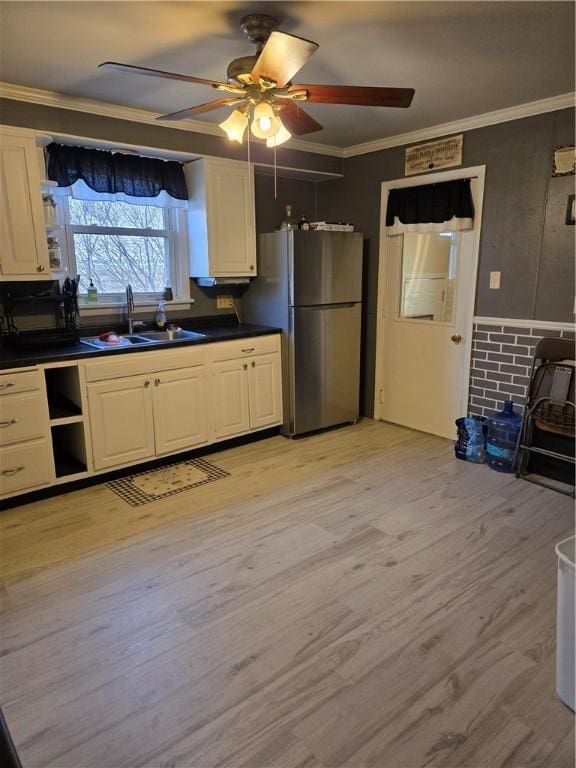 kitchen featuring a sink, ornamental molding, light wood-type flooring, freestanding refrigerator, and dark countertops