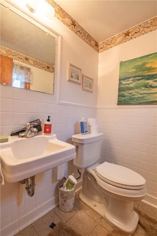 bathroom with a wainscoted wall, tile walls, toilet, a sink, and tile patterned floors